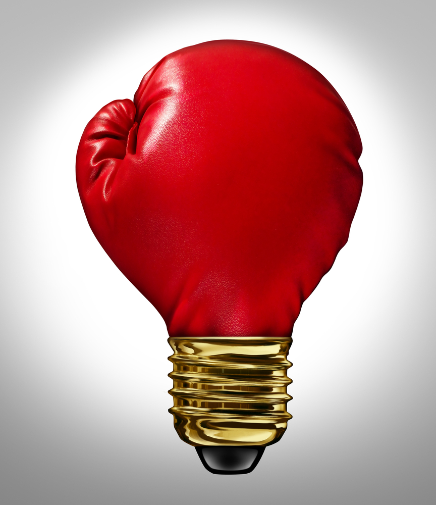 Creative power and Powerful ideas business innovation concept with a red glowing boxing glove shaped as a light bulb representing strong innovative new thinking and competitive imagination.
