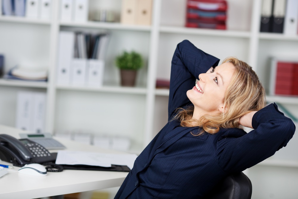 Happy-businesswoman-relaxing-with-hands-behind-head-at-office-desk