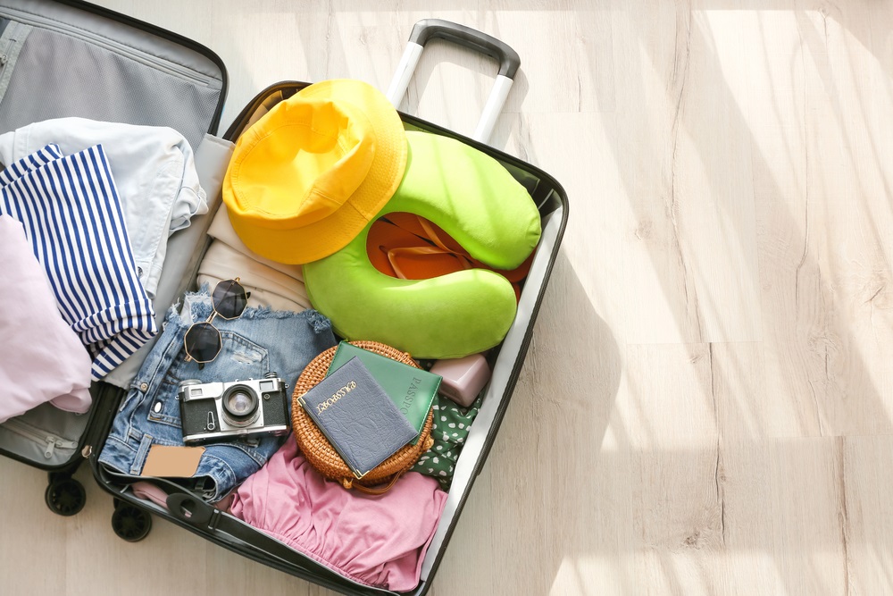 Opened suitcase with clothes and different accessories for travelling on light wooden floor