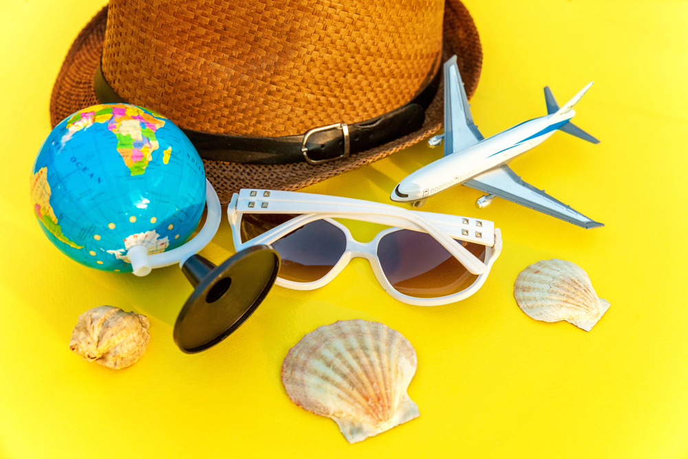 Concept of time off on bright yellow background including vacation hat, airplane, sunglasses shells and a globe